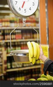 Man&acute;s hand weighing a bunch of bananas on a weighing scale in a supermarket
