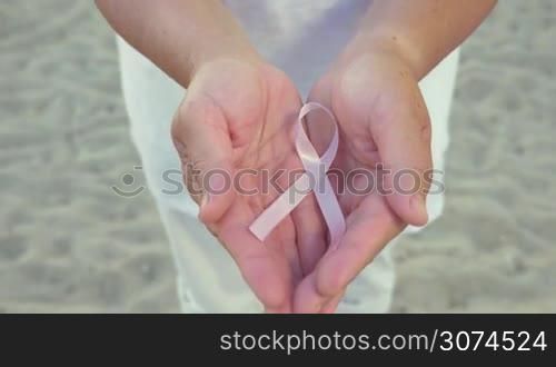 Man&acute;s hands holding pink bow symbolizes cancer sign. Unrecognizable.