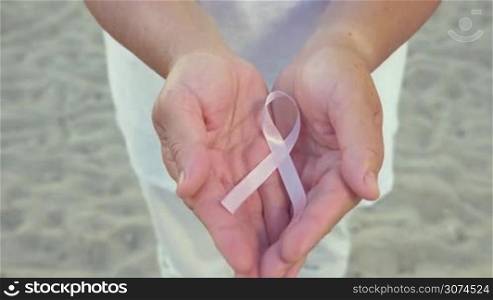 Man&acute;s hands holding pink bow symbolizes cancer sign. Unrecognizable.