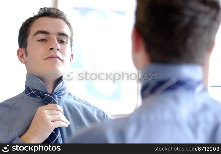 man adjusting tie in mirror
