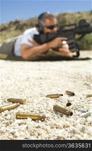 Man aiming machine gun at firing range, focus on bullets in foreground