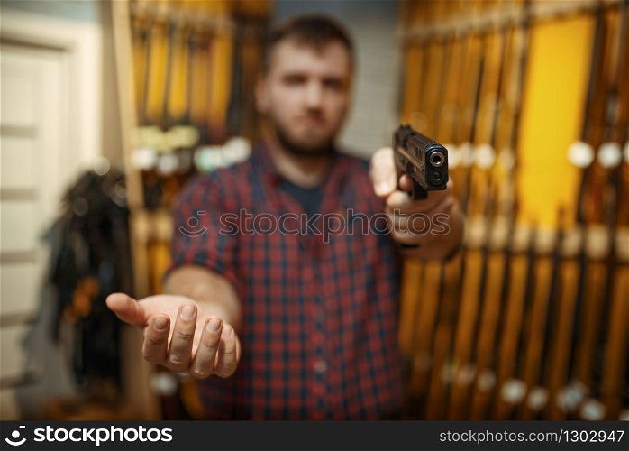 Man aims with new handgun in camera, gun shop. Male person buying pistol for security in weapon store, selfdefence and sport shooting hobby. Man aims with new handgun in camera, gun shop