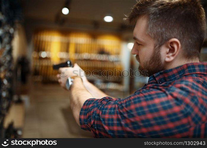 Man aims with new handgun in gun shop. Male person buying pistol for security in weapon store, selfdefence and sport shooting hobby. Man aims with new handgun in gun shop