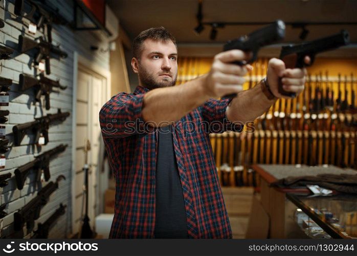 Man aims with two handguns in gun shop. Male person buying pistol for security in weapon store, selfdefence and sport shooting hobby. Man aims with two handguns in gun shop