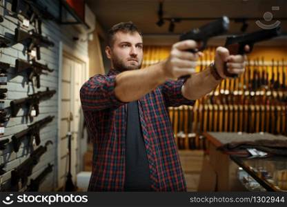 Man aims with two handguns in gun shop. Male person buying pistol for security in weapon store, selfdefence and sport shooting hobby. Man aims with two handguns in gun shop