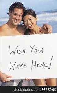 Man &amp; woman Asian couple, boyfriend and girlfriend in bikini, on vacation beach holding Wish You Were Here sign