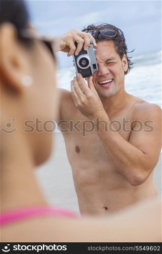 Man &amp; woman couple, boyfriend taking vacation photograph of his girlfriend in a bikini at the beach using a digital camera