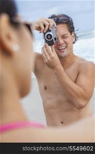 Man &amp; woman couple, boyfriend taking vacation photograph of his girlfriend in a bikini at the beach using a digital camera