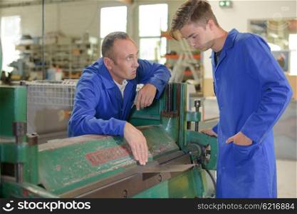 Man and apprentice by industrial machine
