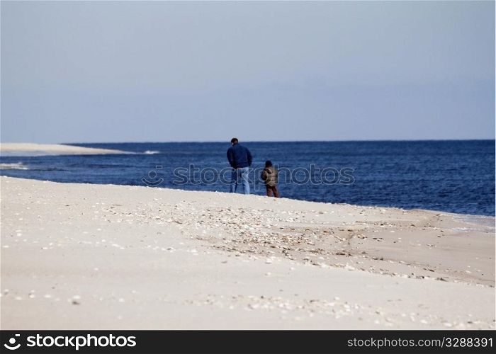 Man and boy on a winter walk on the beach, man&rsquo;s hands in his pocket, striding in the cold weather;