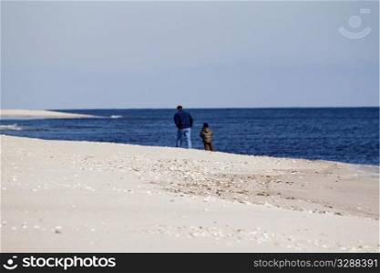 Man and boy on a winter walk on the beach, man&rsquo;s hands in his pocket, striding in the cold weather;