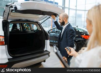 Man and female seller looking auto in car dealership. Customer and saleswoman in vehicle showroom, male person buying transport, automobile dealer business. Man and female seller looking auto, car dealership