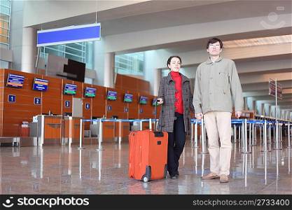 man and girl with red suitcase standing in airport hall looking at camera