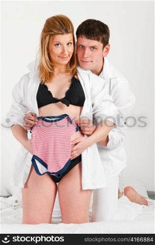 man and his pregnant wife are trying baby clothes on her belly