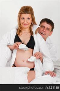 man and his pregnant wife are trying baby shoes on her belly