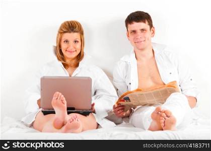 man and his pregnant wife in bed at morning with laptop and newspaper
