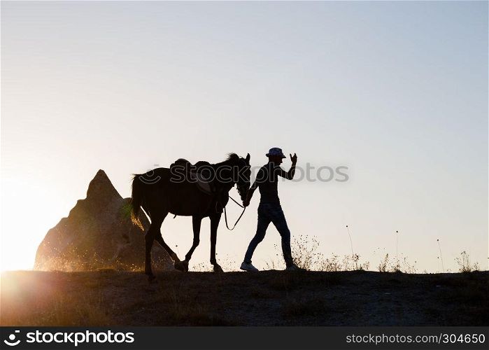 Man and horse silhouette in valley at Cappadocia,Anatolia,Turkey.Fairy tale chimneys in Cappadocia, tourist attraction places in Goreme, Cappadocia, Turkey. Man and horse silhouette on the background of valley at Cappadocia,Anatolia,Turkey.The great tourist attraction of Cappadocia best places to fly with hot air balloons.Rocks looking like mushrooms.