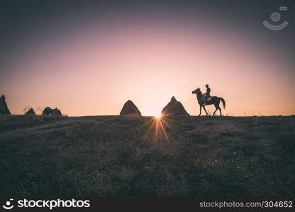 Man and horse silhouette in valley at Cappadocia,Anatolia,Turkey.Fairy tale chimneys in Cappadocia, tourist attraction places in Goreme, Cappadocia, Turkey. Man and horse silhouette on the background of valley at Cappadocia,Anatolia,Turkey.The great tourist attraction of Cappadocia best places to fly with hot air balloons.Rocks looking like mushrooms.