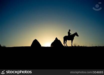 Man and horse silhouette in valley at Cappadocia,Anatolia,Turkey.Fairy tale chimneys in Cappadocia, tourist attraction places in Goreme, Cappadocia, Turkey. Man and horse silhouette on the background of valley at Cappadocia,Anatolia,Turkey.The great tourist attraction of Cappadocia best places to fly with hot air balloons.Rocks looking like mushrooms.