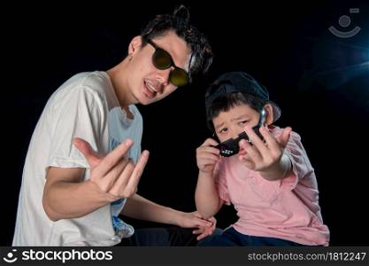 Man and little boy with sunglasses sit looking camera on dark studio background , asian family
