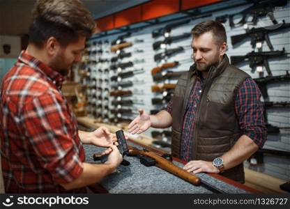 Man and owner choosing rifle and handgun in gun shop. Euqipment for hunters in weapon store, hunting and sport shooting hobby, security and selfdefence. Man with owner choosing handgun in gun shop