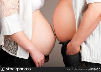 man and pregnant woman is showing their bellies, side view