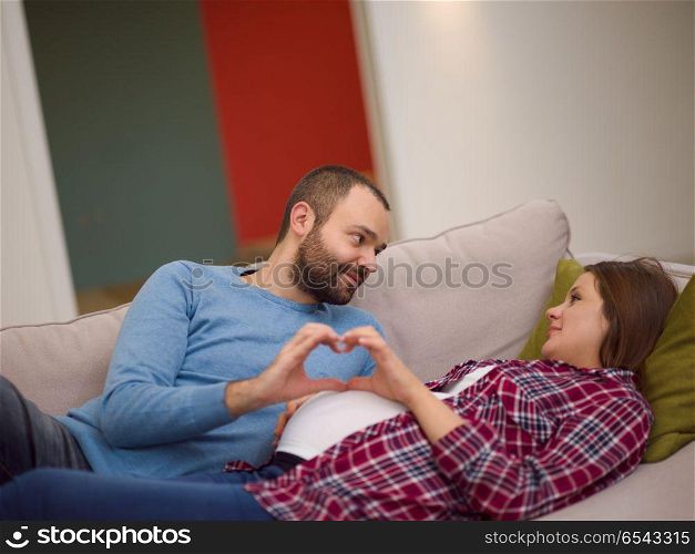man and pregnant woman showing heart sign. Happy man and pregnant woman showing heart sign with fingers while relaxing on the sofa at home
