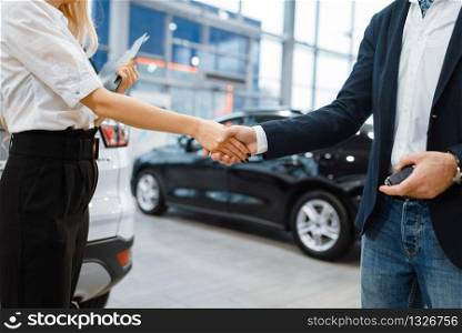 Man and saleswoman shake hands in car dealership. Customer and seller in vehicle showroom, male person buying transport, auto dealer business. Man and saleswoman shake hands in car dealership