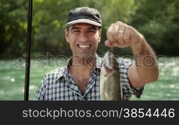 Man and sport, mid adult fisherman on holidays on river, relaxing and fishing trout, smiling and showing fish to the camera. Part 1 of 8
