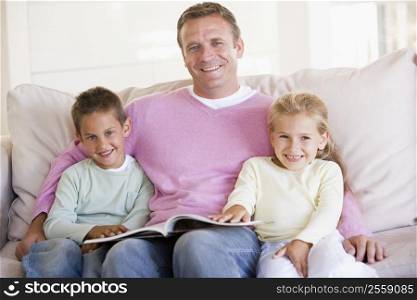 Man and two children sitting in living room reading book and smiling