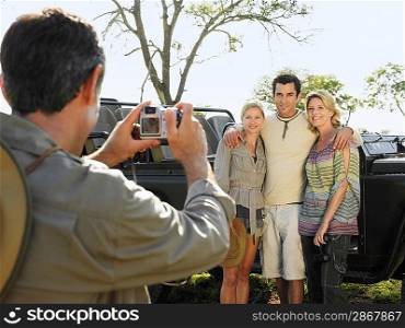 Man and two women posing by jeep man taking photograph