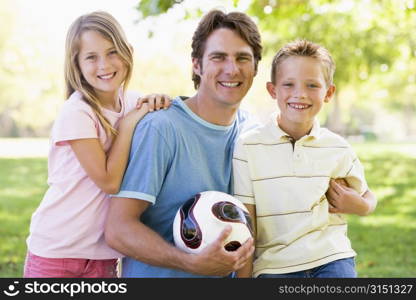 Man and two young children outdoors holding volleyball and smiling