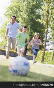 Man and two young children outdoors playing soccer and having fun