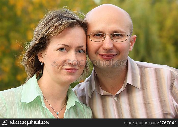 man and woman are cuddling in early fall park and looking at camera