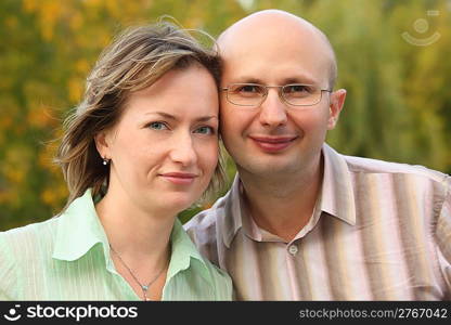 man and woman are cuddling in early fall park and looking at camera