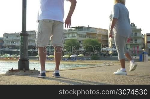 Man and woman are doing morning exercises by the water, they are stretching leg muscles.