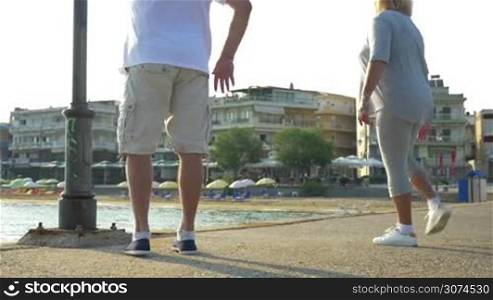 Man and woman are doing morning exercises by the water, they are stretching leg muscles.