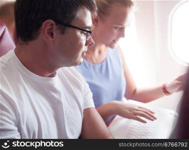 Man and woman are sitting by and watching something in laptop during the flight.