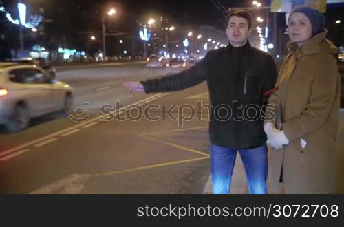 Man and woman are standing on the roadside and talking. Man is thumbing a ride.