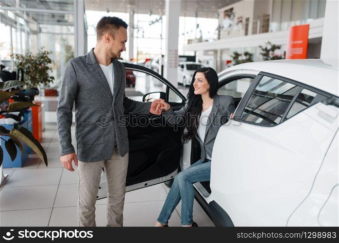 Man and woman buying new car in showroom. Male and female customers choosing vehicle in dealership, automobile sale, auto purchase