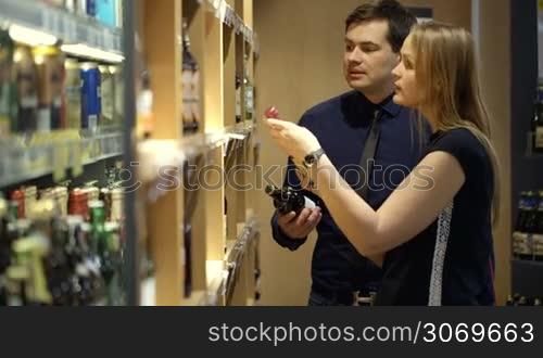 Man and woman choosing a bottle of wine in the shop. Woman checking prices