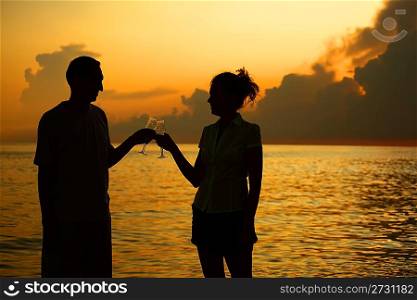 Man and woman clink glasses. Silhouettes against sea.