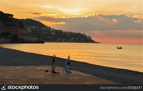 Man and woman doing gymnastics on the beach of Nice, at sunrise, France