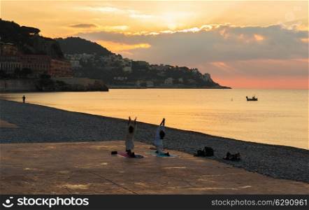 Man and woman doing gymnastics on the beach of Nice, at sunrise, France