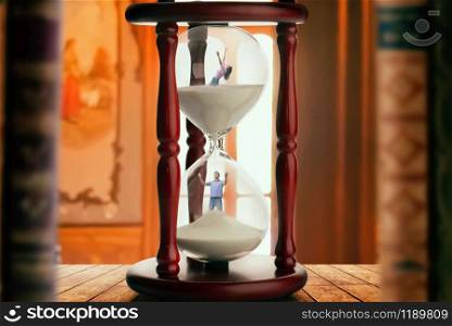 Man and woman drowning inside an hourglass, deadline concept, bookshelf on background. Man and woman inside hourglass, deadline concept