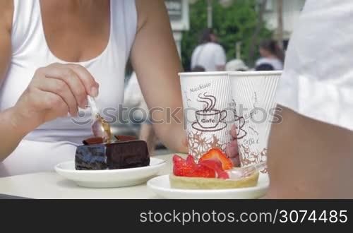 Man and woman eating chocolate and strawberry desserts and drinking coffee. Sweet toothers enjoying delicious cakes in outdoor cafe