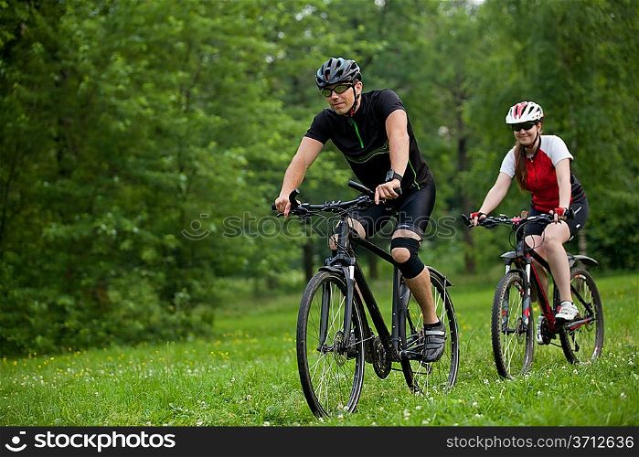 Man and woman exercising with bicycles outdoors, they are a couple in forest