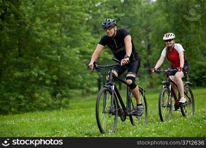 Man and woman exercising with bicycles outdoors, they are a couple in forest