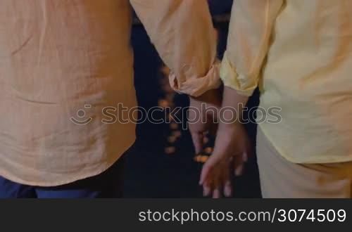 Man and woman holding hands against of sea in moon light. Unrecognizable.