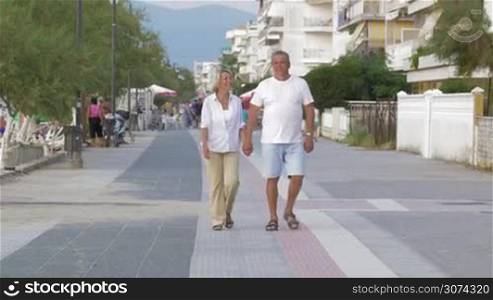 Man and woman holding hands and talking while walking down the street on holiday.